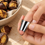Close-up of a stainless steel finger guard being fitted onto a finger beside roasted chestnuts